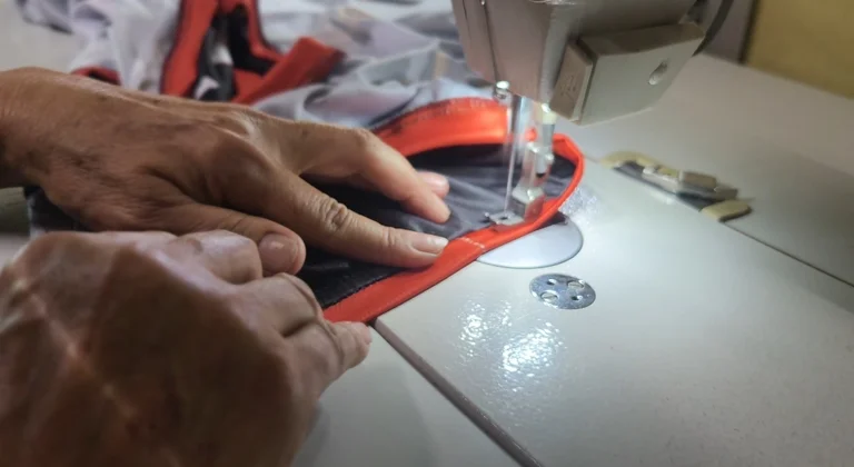 Hands guiding orange trim under the needle of a sewing machine